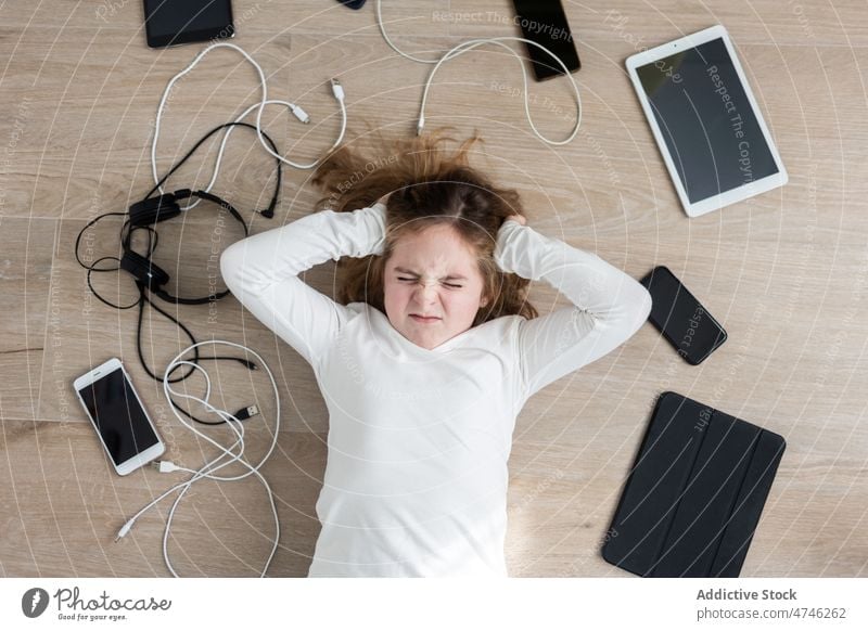 Aufgeregtes Mädchen inmitten verschiedener Gadgets verärgert Apparatur Kabel Abhängigkeit Sucht Bestrafung traurig unglücklich verbieten modern Problematik