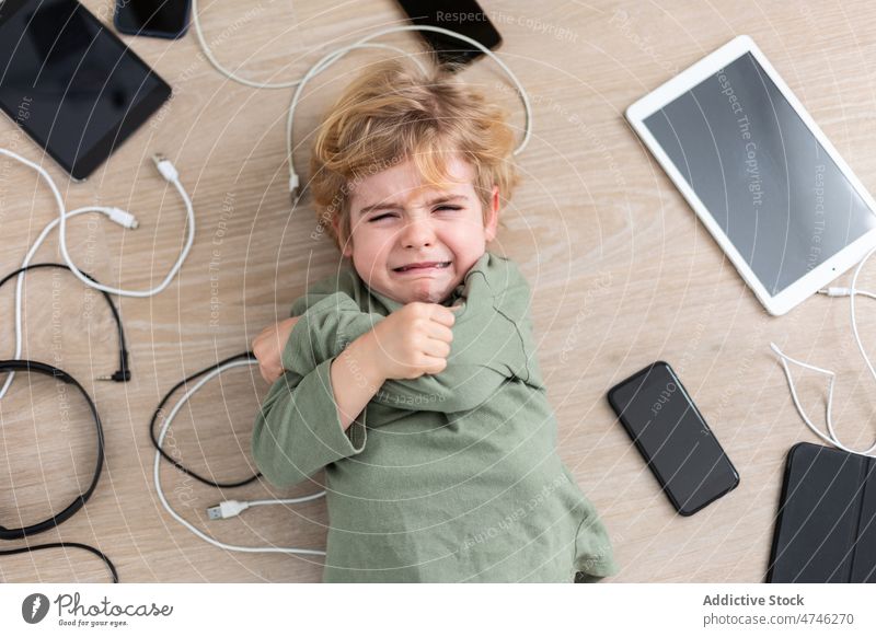 Weinender Junge inmitten diverser Gadgets weinen verärgert Apparatur Kabel Abhängigkeit Sucht Bestrafung unglücklich verbieten modern Problematik Gerät Kind