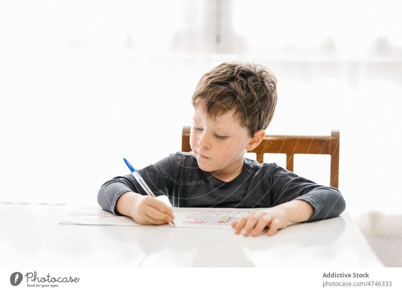 Junge schreibt auf Papier am Tisch Kind lernen schreiben Hausaufgabe Wissen Bildung primär Kognition heimwärts klug sorgsam Schreibtisch Fokus