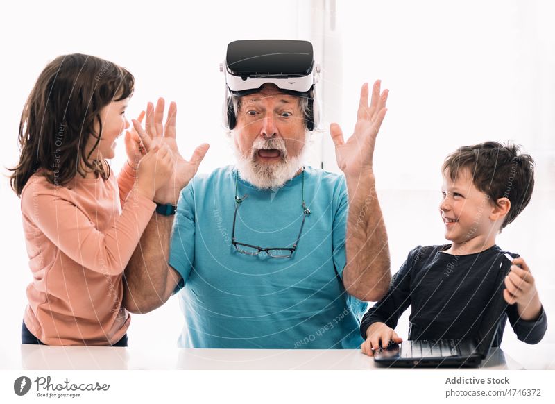 Erstaunlicher Großvater mit VR-Brille in der Nähe von Kindern erkunden Cyberspace futuristisch eintauchen Laptop Erstaunen Spaß haben Virtuelle Realität Netbook