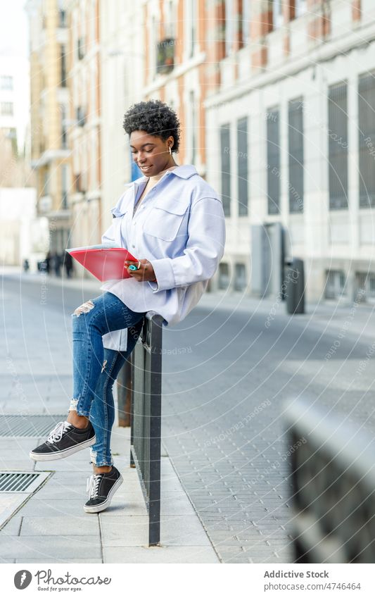 Lächelnde schwarze Frau liest Dokumente auf der Straße Schüler Großstadt urban feminin Schriftstück lesen Information Wissen positiv Afroamerikaner heiter Dame