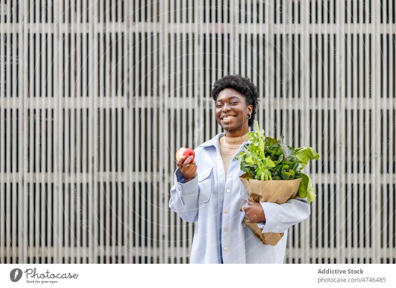 Zufriedene schwarze Frau mit Einkaufstüte und Apfel Straße Suppengrün gesunde Ernährung organisch Lächeln Vitamin Lebensmittelgeschäft Frucht Glück Kauf
