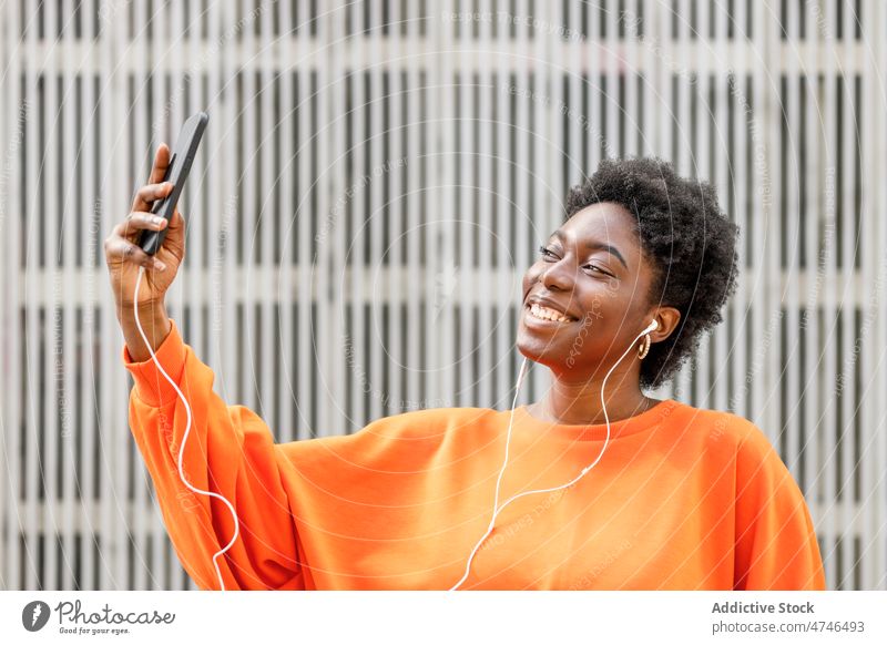 Fröhliche schwarze Frau, die Musik hört und ein Selfie macht Kopfhörer meloman Gesang Straße Smartphone soziale Netzwerke Selbstportrait einfangen Gedächtnis