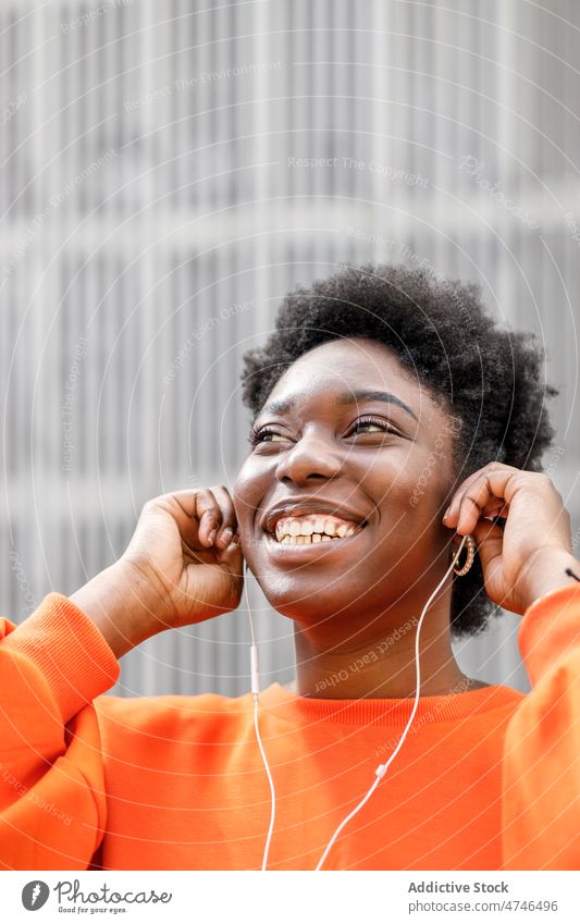 Fröhliche schwarze Frau beim Musikhören Kopfhörer meloman Gesang Wiedergabeliste Straße Großstadt Melodie Zeitvertreib Audio Vorschein Stil feminin urban