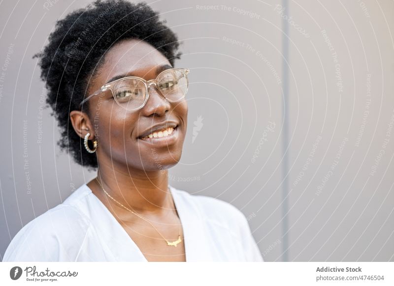 Zufriedene schwarze Frau mit Brille und Arbeitsuniform Straße Großstadt Vorschein Stil feminin urban Wand Uniform Afroamerikaner Sommer froh weiß genießen