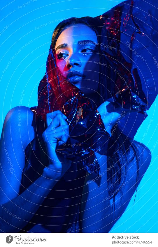 Modische Frau in Plastik eingewickelt in Neonbeleuchtung Model neonfarbig provokant cool Kunststoff Körperhaltung Make-up umhüllen Stil blau Licht leuchten
