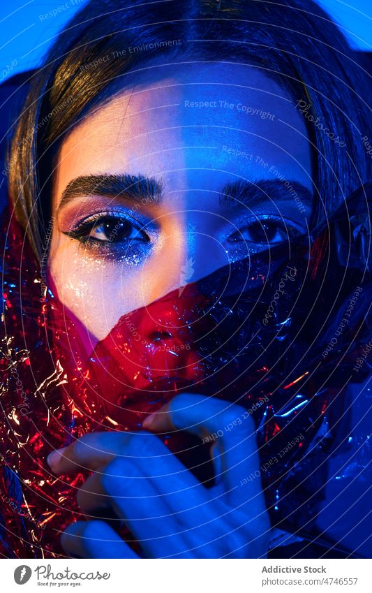 Modische Frau in Plastik eingewickelt in Neonbeleuchtung Model neonfarbig provokant cool Kunststoff Körperhaltung Make-up umhüllen Stil blau Licht leuchten