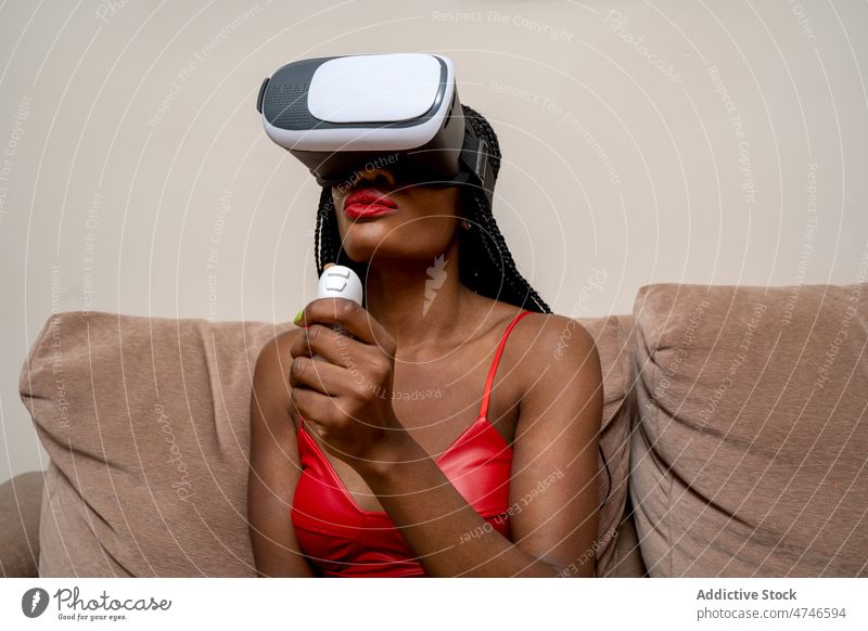 Schwarze Frau mit VR-Brille Headset Regler Cyberspace futuristisch erkunden simulieren eintauchen Wohnzimmer Erfahrung Virtuelle Realität Schutzbrille