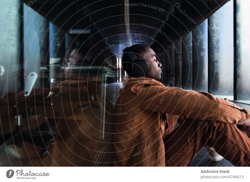 Schwarzer Mann hört Musik in der Nähe eines Gebäudes Kopfhörer Straße Stil Gesang Melodie Zeitvertreib Hobby schwarz Afroamerikaner Glaswand männlich zuhören