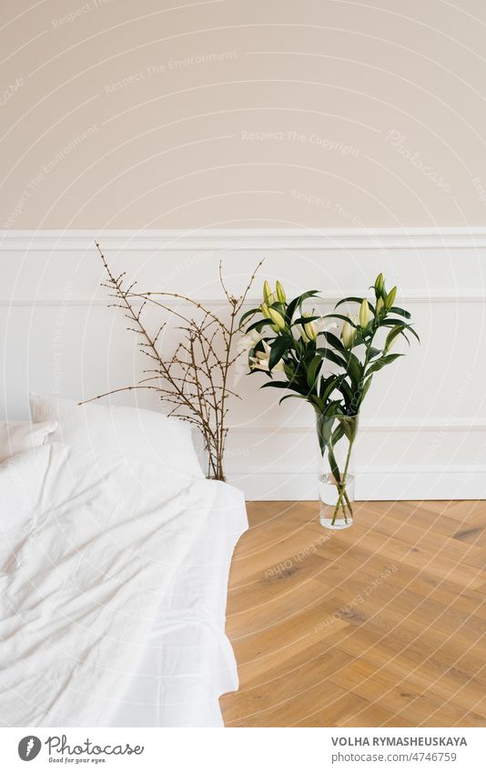 Weiße Lilienblüten in einer Vase, Baumzweige in einer Vase neben dem Bett. Details der Inneneinrichtung des Hauses Appartement Schlafzimmer Komfort bequem
