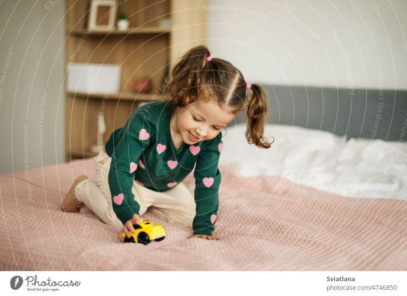 Ein charmantes kleines Mädchen spielt mit einem Auto auf dem Bett. Home Spiele, Kind Entwicklung Heimspiele Baby Spielzeug Spielen niedlich Kinder Hintergrund