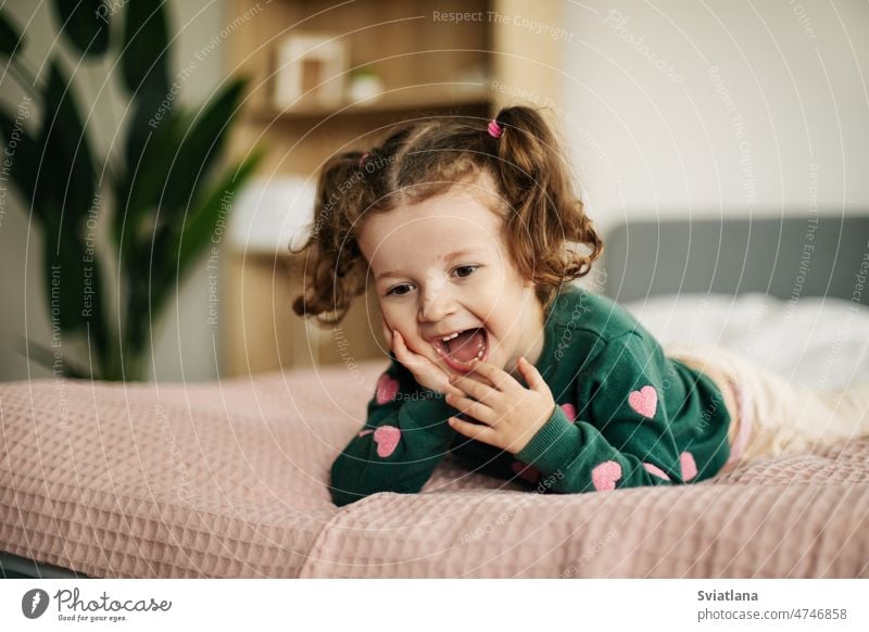 Ein emotionales kleines Mädchen spielt auf dem Bett im Schlafzimmer und lacht wenig Spaß Frau niedlich Kind Morgen Porträt Behaarung im Innenbereich Gesicht Tag
