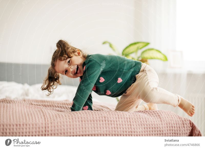 Ein bezauberndes kleines Mädchen springt auf das Bett und lacht wenig Spaß Frau niedlich Kind Morgen Porträt Behaarung im Innenbereich Gesicht emotional Tag