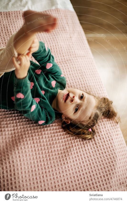 Ein niedliches kleines Mädchen liegt auf dem Bett mit angehobenem Bein und streckt ihr Höschen wenig Spaß Frau Kind Morgen Porträt Behaarung im Innenbereich