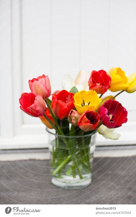 Ein bunter Tulpenstrauss in einer Glasvase steht auf einer Steinstufe vor einer weißen Türe Blüte Strauss Blumenstrauß Ostern Frühling grün Blühend schön