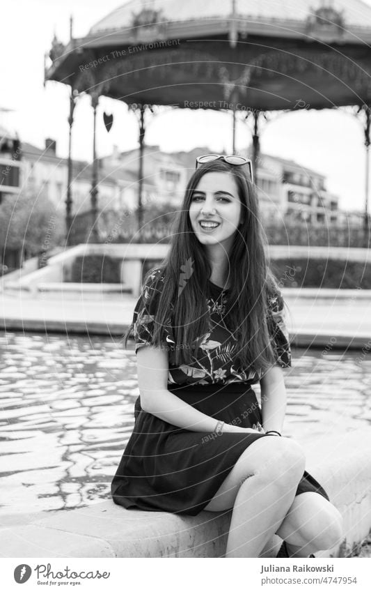 Junge Frau mit langen Haaren sitzt am Brunnen sitzen einzigartig trendy Freundlichkeit authentisch T-Shirt Model hübsch Mädchen träumen langhaarig Lifestyle