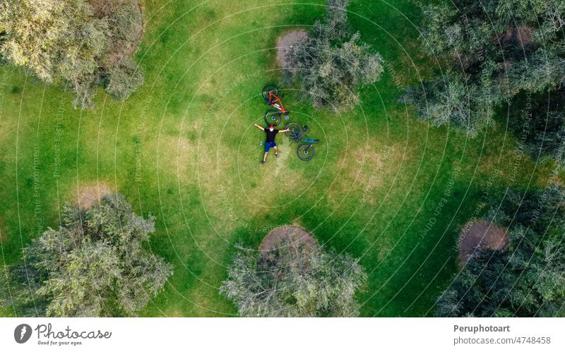 Drohnenaufnahme eines Radfahrers, der auf einer Wiese liegt und sich ausruht. Mann Dröhnen Park Radfahren Baum genießend Fahrrad oben Hintergrund Muster Sport