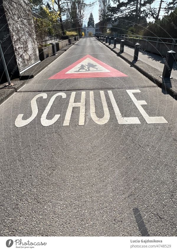 Warnschild für den Schulweg in deutscher Sprache in der Schweiz. Straßenschild ist rotes Dreieck mit laufenden Kindern in weißem Feld und Text Schule, die Schule bedeutet.
