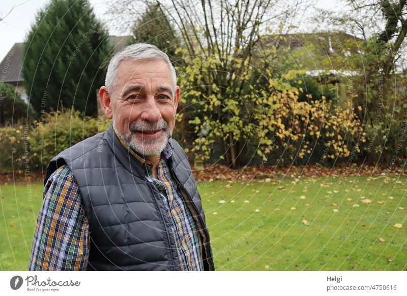 Porträt eines Senioren, der im Garten steht und lächelt Mensch Mann grauhaarig kurzhaarig Bart Lächeln Freundlichkeit freundlich Wiese Sträucher Herbst draußen