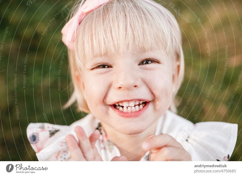 Porträt eines kleinen lachenden schönen Mädchens in der Natur am Sommertag Urlaub. Kind im Kleid spielt im grünen Park in der sonnigen Zeit. Das Konzept der Familienurlaub und Zeit zusammen