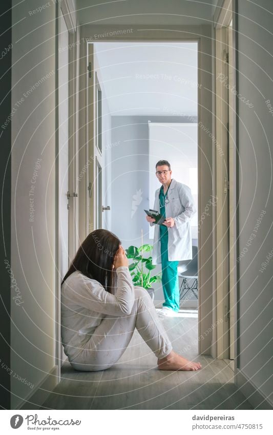 Arzt betrachtet eine Patientin mit einer psychischen Störung, die auf dem Boden in einem psychiatrischen Zentrum sitzt arzt Blick geduldig Frau Pyjama mental