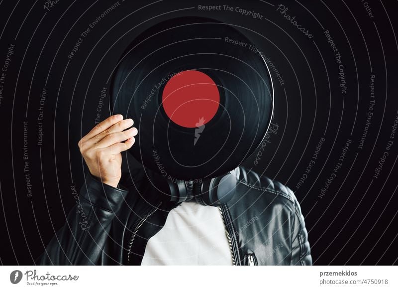 Mann versteckt sich hinter einer Retro-Schallplatte, die den Kopf bedeckt. Rock-Stil. Vintage-Musik-Stil. Mann in schwarzer Jacke mit Schallplatte auf schwarzem Hintergrund. Retro-Musik
