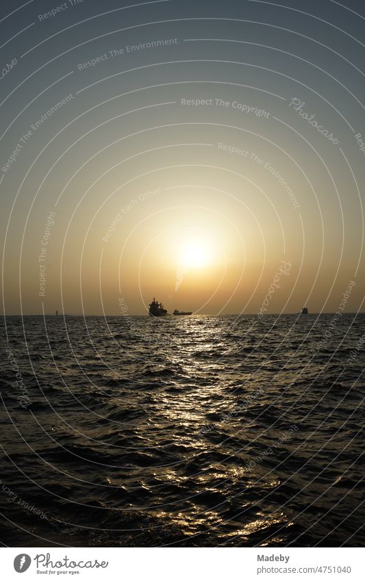 Ankerndes Frachtschiff in der Bucht von Izmir im Licht der untergehenden Sonne über dem Ägäischen Meer im Sommer in der Türkei Heimkehr Kitsch Abend Welthandel