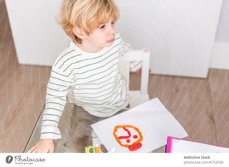 Junge macht trauriges Gesicht mit roter Knetmasse auf weißem Papier Kind Knetgummi Diagnostik Kindheit besuchen wählen Stimmung Raum Ernennung mental Licht