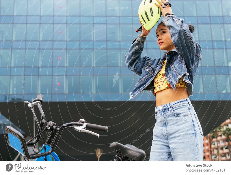Ethnische Frau setzt Helm auf, um Fahrradfahren zu üben angezogen Schutzhelm Aktivität modern Stil Freizeit Hobby Zeitvertreib vorbereiten Verkehr Sicherheit