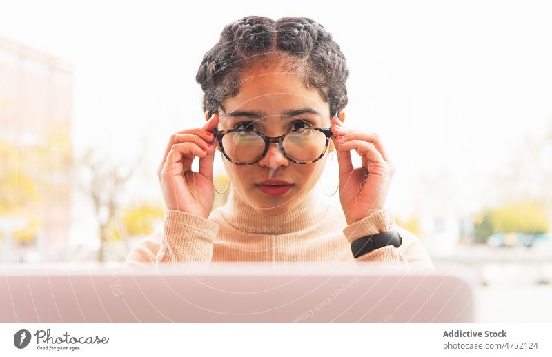 Junge ethnische Frau, die eine Brille trägt, um am Laptop zu arbeiten angezogen freiberuflich benutzend Stil abgelegen Arbeitsplatz praktisch ernst unabhängig