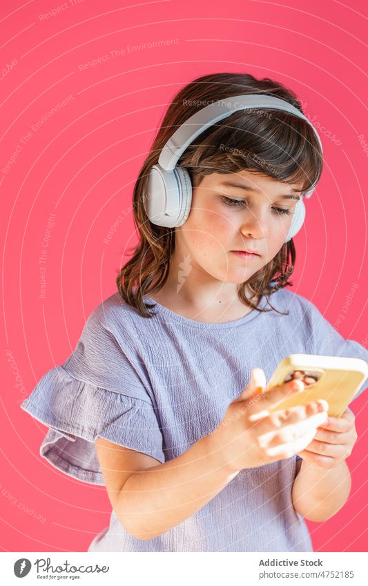 Kleines Mädchen, das mit Kopfhörern Musik hört und eine Nachricht liest benutzend Drahtlos zuhören Suche Smartphone hell Gesang Wiedergabeliste digital Browsen