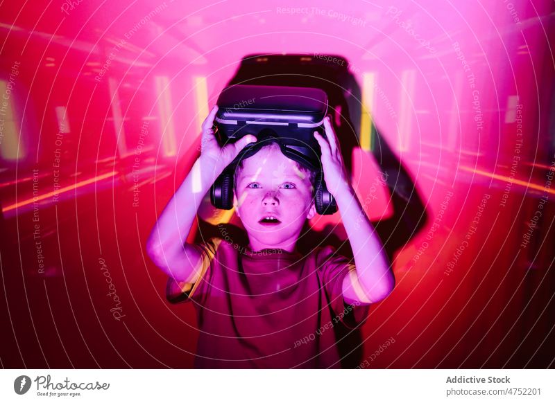 Erstaunter Junge nimmt VR-Helm ab Spieler Schock Headset Abheben neonfarbig leuchten Videospiel erkunden Virtuelle Realität hell erstaunt Kind unterhalten Gerät
