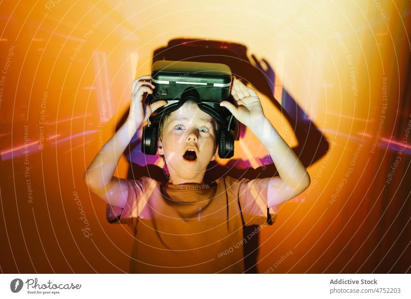 Erstaunter Junge nimmt VR-Helm ab Spieler Schock Headset Abheben neonfarbig leuchten Videospiel erkunden Virtuelle Realität hell erstaunt Kind unterhalten Gerät