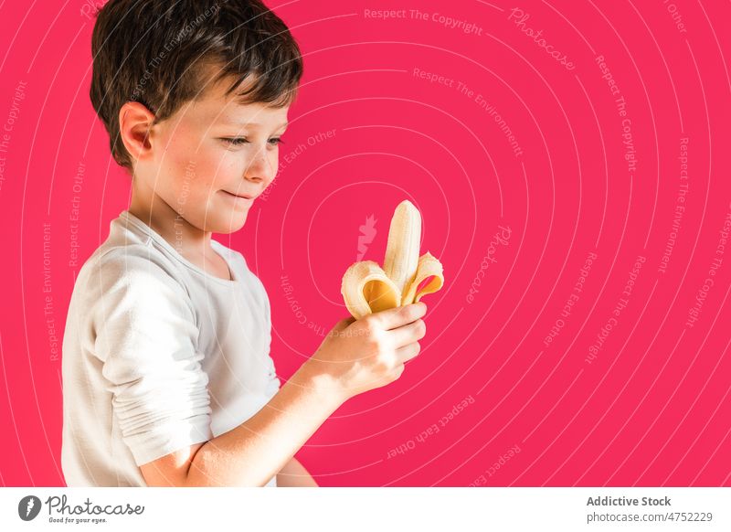 Niedlicher Junge mit frischer Banane in hellem Studio Kind essen süß Frucht lebhaft lecker gesunde Ernährung Lächeln positiv sich[Akk] schälen geschmackvoll