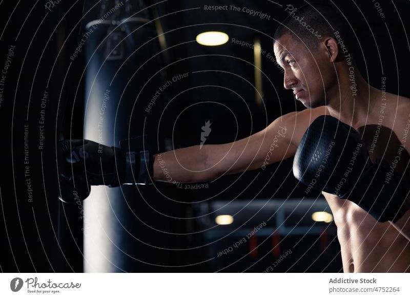 Hemdloser hispanischer Sportler beim Boxen im Fitnessstudio Bowle Tasche Boxsport Porträt Training stark Handschuh Kraft Boxer männlich ohne Hemd intensiv