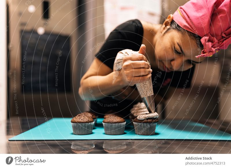 Hispanische Frau drückt Sahne auf Muffins Bäcker dekorieren Cupcake Backwarenbeutel Bäckerei Tisch drücken Dessert Gebäck süß Schokolade Küche kulinarisch