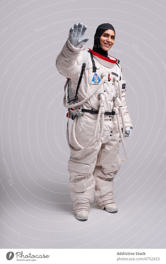 Lächelnder ethnischer Astronaut winkt mit der Hand in die Kamera Mann Raumanzug Abschied Missionsstation bereit Wellenhand erkunden Astronomie Fundstück Latein