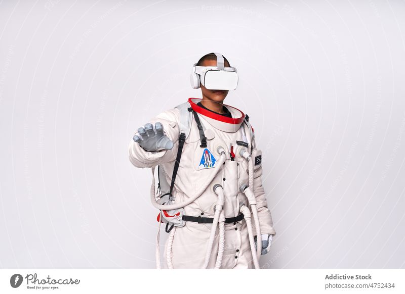 Ethnischer Astronaut in Raumanzug und VR-Brille im Studio Mann Metaversum Schmuckkörbchen Schutzbrille interagieren erkunden Virtuelle Realität simulieren