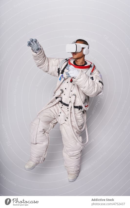 Ethnischer Astronaut in Raumanzug und VR-Brille im Studio Mann Schmuckkörbchen Schutzbrille interagieren erkunden Virtuelle Realität Metaversum simulieren