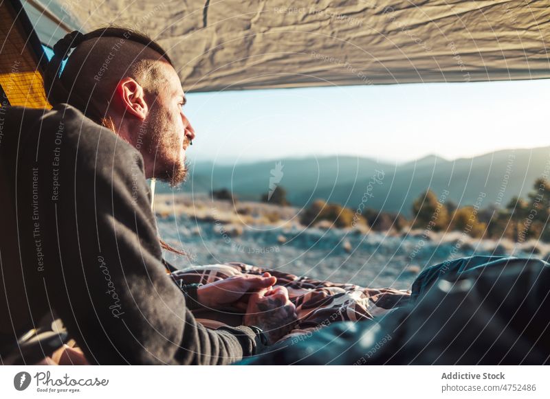 Bärtiger männlicher Wanderer genießt die Natur vom Zelt aus bei Sonnenaufgang Mann Lager Hügel bewundern Trekking Abenteuer sich[Akk] entspannen Reisender