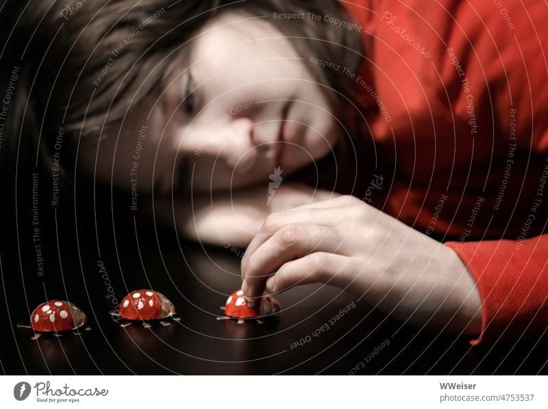 Ein Mädchen hat den Kopf traurig auf den Arm gelegt und spielt verträumt mit Glückskäfern Kind Kindheit nachdenklich versonnen langweilig gelangweilt Schokolade
