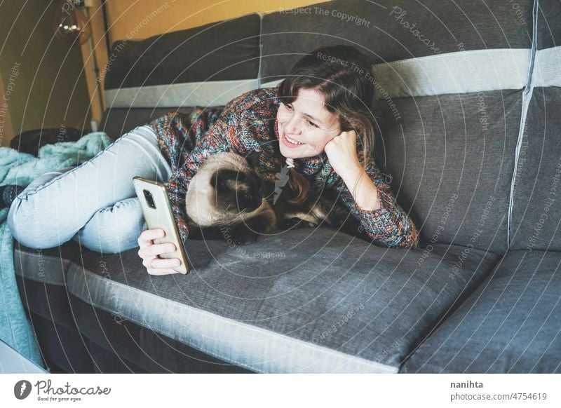 Junge Frau zu Hause, die sich mit ihrem Haustier ausruht Telearbeit Single Katze soziale Netzwerke aussruhen heimwärts siamesisch Liebe Familie Routine