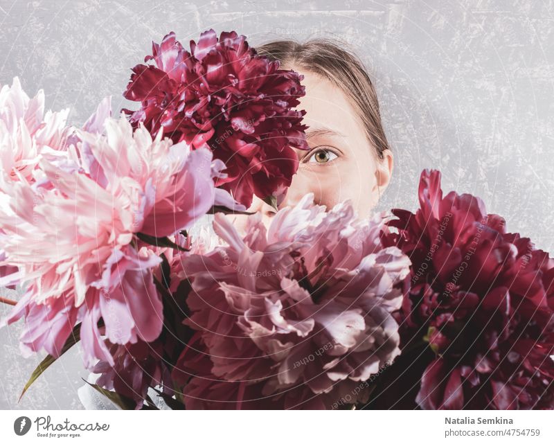Große unscharfe Bouquet von rosa Pfingstrosen Abdeckung Gesicht junge Frau auf grauem Hintergrund. Fokus sind auf einem ihr Auge. kreativ retro gesichtslos