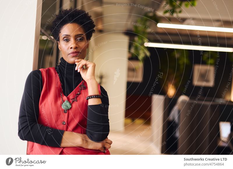Porträt einer reifen schwarzen Frau mit Hand am Kinn, die mit nachdenklichem Gesichtsausdruck in einem Coworking Space in die Kamera schaut Geschäftsfrauen