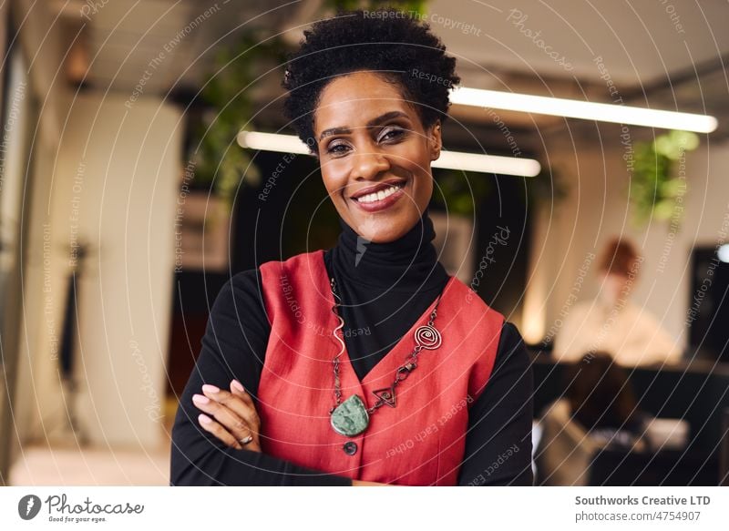 Porträt einer fröhlichen reifen schwarzen Frau mit verschränkten Armen, die in die Kamera schaut und lächelt, im Coworking Space Ermächtigung heiter Waffen