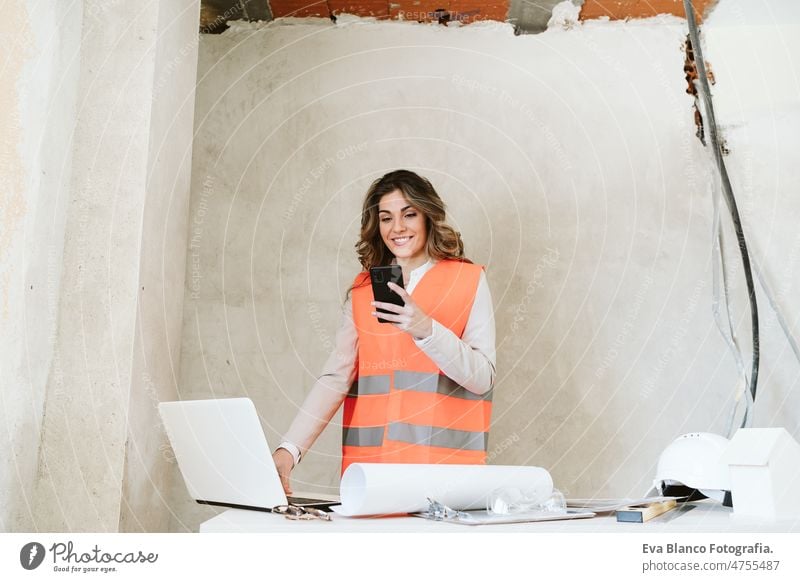 Professionelle selbstbewusste Architektin auf einer Baustelle, die ein Mobiltelefon benutzt und Baupläne hält Frau Blaupausen Arbeitsbereich Schutzhelm
