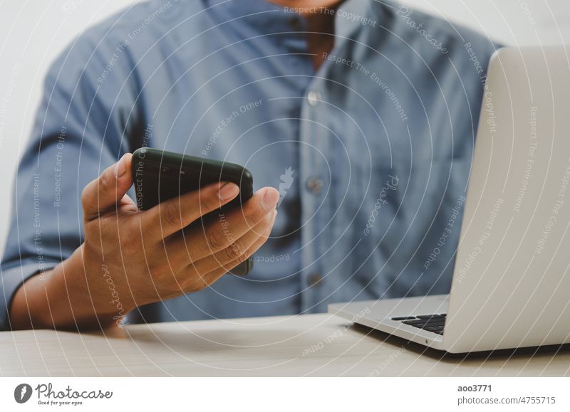 Ein Mann, der ein Smartphone und einen Laptop benutzt, um im Internet zu suchen, SMS zu versenden, einen SMS-Messenger zu benutzen oder Online-Banking zu betreiben.
