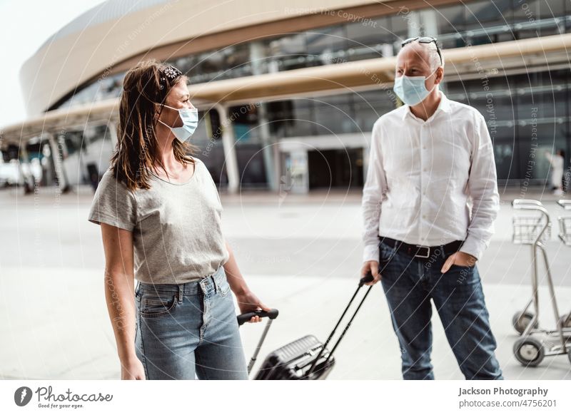 Reisende mit Schutzmasken unterhalten sich beim Verlassen des Flughafens mit ihrem Gepäck reisen Pandemie Mundschutz Frau Mann plaudernd Talkrunde reden Junge