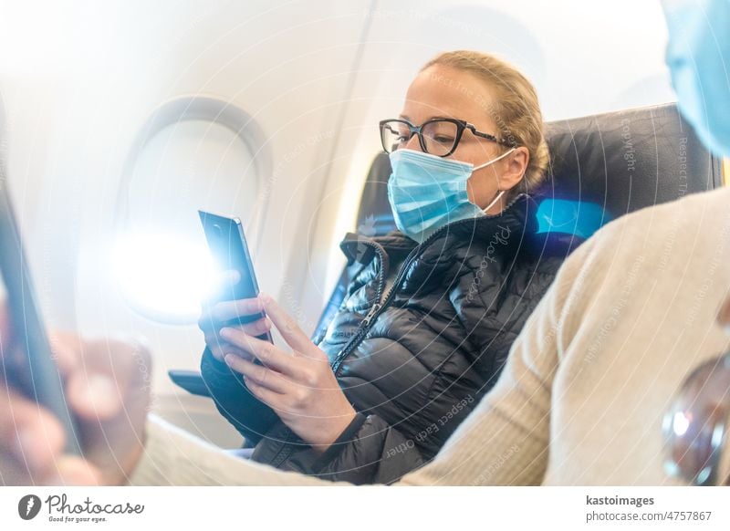 Ein junges Paar trägt eine Gesichtsmaske und benutzt ein Smartphone, während es im Flugzeug reist. Neue normale Reise nach Covid-19 Pandemie Konzept. reisen