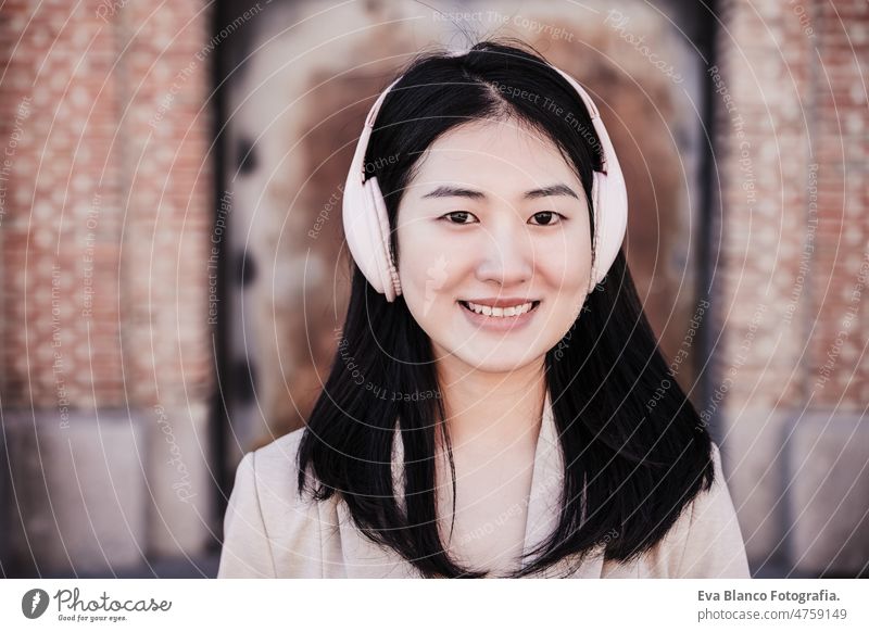 Nahaufnahme einer lächelnden Frau, die mit Kopfhörern und Mobiltelefon in der Stadt Musik hört Glück Chinesisch Großstadt Handy Lächeln Überfahrt Straße urban